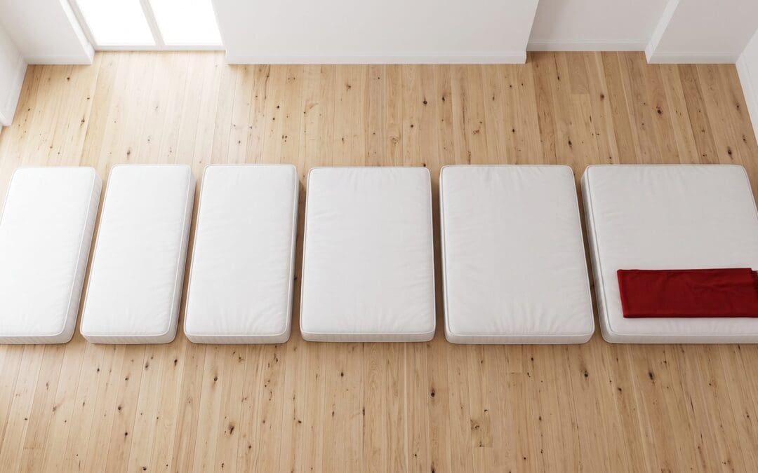 Six white mattresses on a timber floor arranged from smallest to largest, showing the Australian mattress sizes from single to king